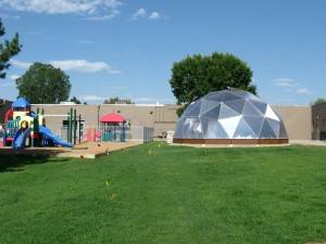 Geodesic Greenhouse in front of a school on the grass next to a playground