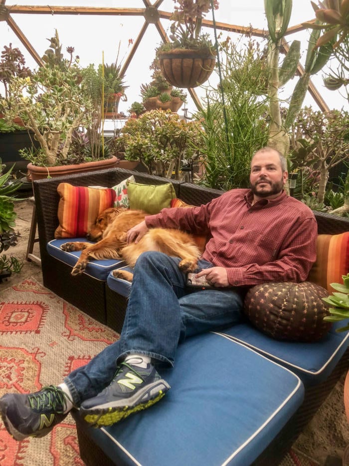 Daniel relaxing in Growing Dome Greenhouse with dog and a variety of succulents