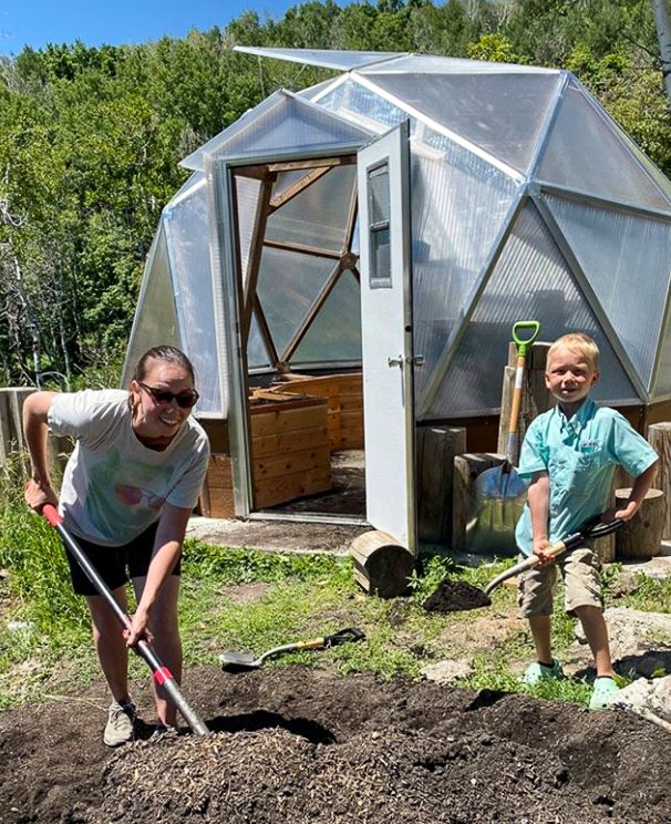 mother and soie digging soil in front of a greenhouse