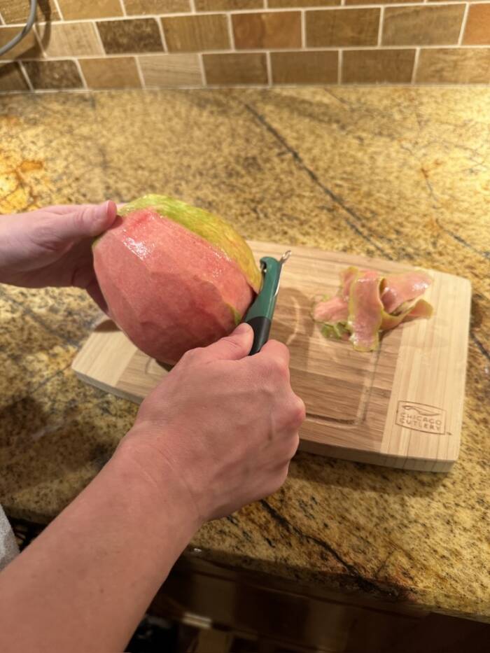 peeling a pink guava on a cutting board with a vegetable peeler