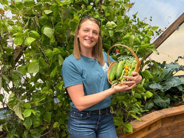 Woman holding a basket of produce grown in a Growing Dome greenhouse