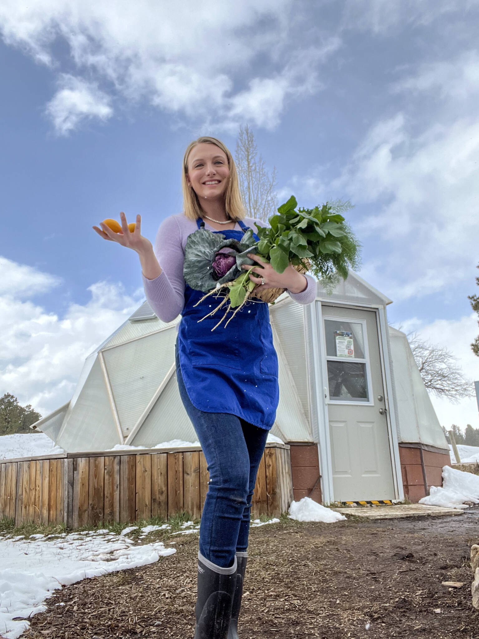 Shelby Lucero in front of an 18' Growing Dome greenhouse holding fresh produce in the winter.