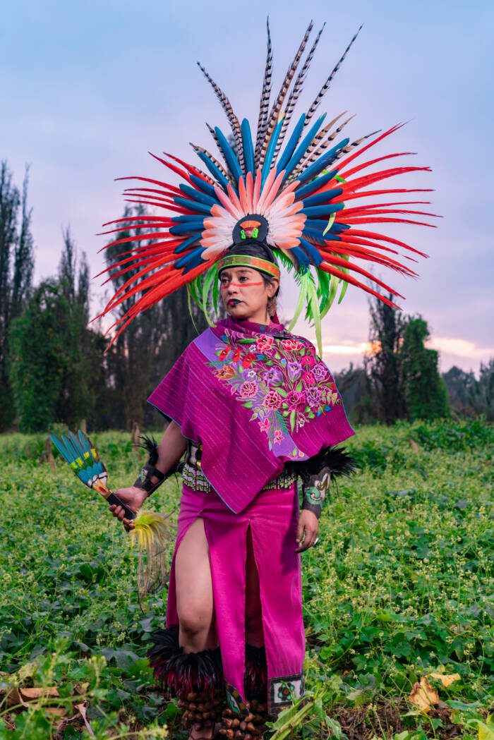 Aztec dancer in the field also known as Chinampa in Xochimilco Mexico with the traditional Aztec clothing and accessories like Penachos or Huipiles - Growing Spaces Greenhouses Aztec dancer in a field also known as "Chinampa" in Xochimilco, Mexico, wearing the traditional Aztec clothing