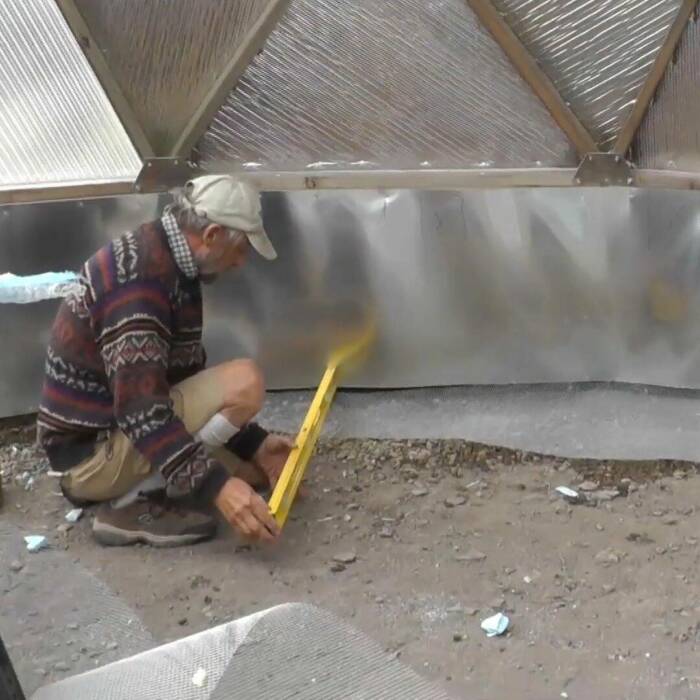 Rodent-Protection-Option - Growing Spaces Greenhouses Man installing 1/4" hardware cloth to a greenhouse floor to prevent burrowing rodents