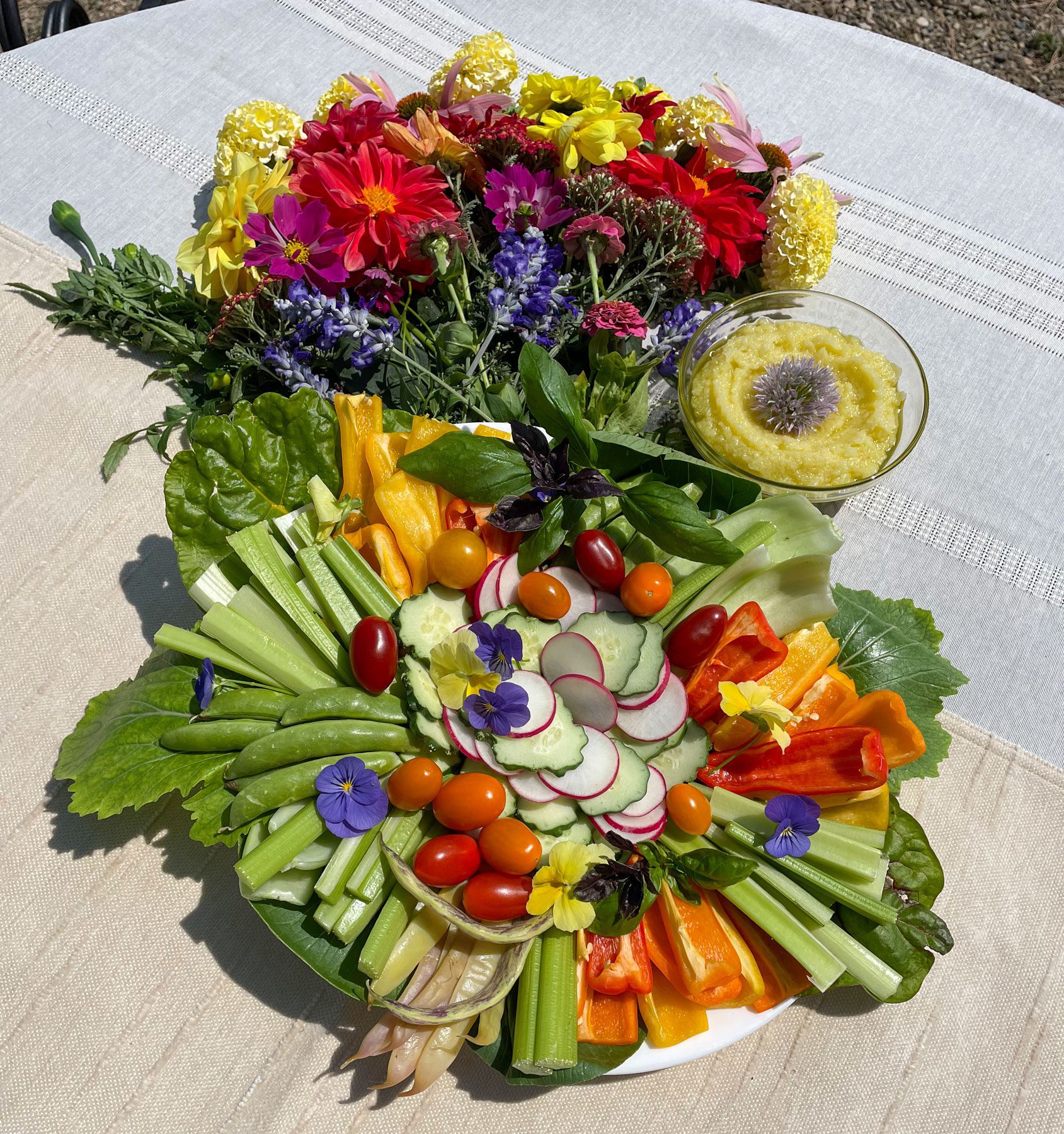 vegetable crudite platter pictured on a white talbecloth with a flower arrangement and garlic toum sauce