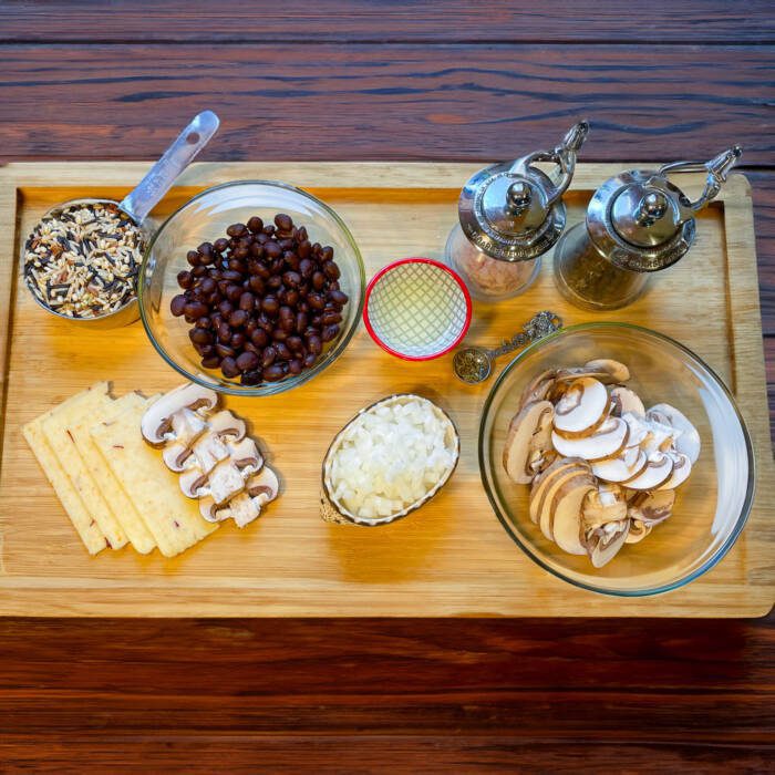 stuffing ingredients on a cutting board cup of dry wild rice, black beans, monterey jack cheese slices, sliced mushrooms, chopped onions, salt and pepper grinders
