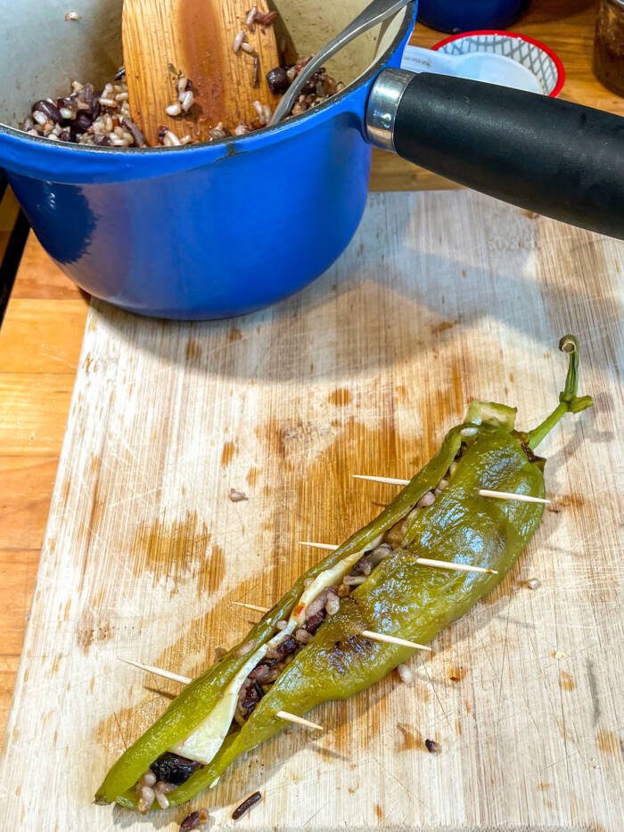 green chile on a cutting board stuffed with cheese and wild rice stuffing and held together with toothpicks blue pot of stuffing in the background