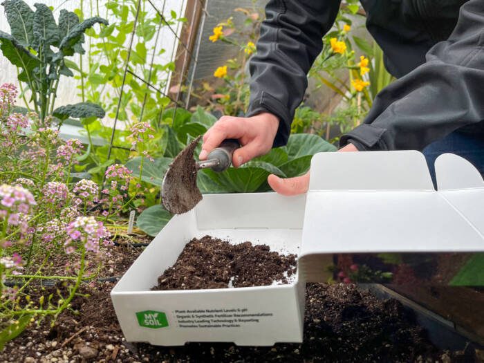 soil_test - Growing Spaces Greenhouses person using a hand trowel to put soil from a raised bed in a test box
