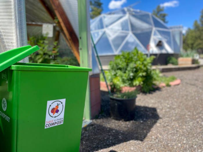 bright green Table to Farm composting bin outside of a geodesic greenhouse
