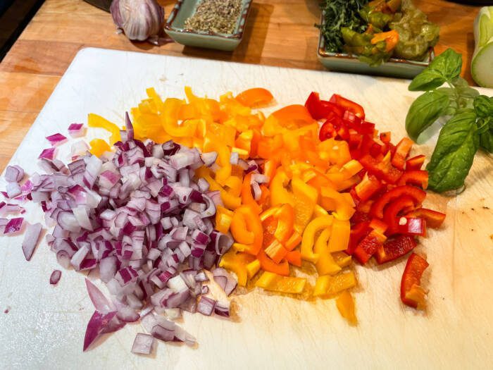 chopped red onions, and red, orange and yellow peppers, fresh basil and herbs on a cutting board
