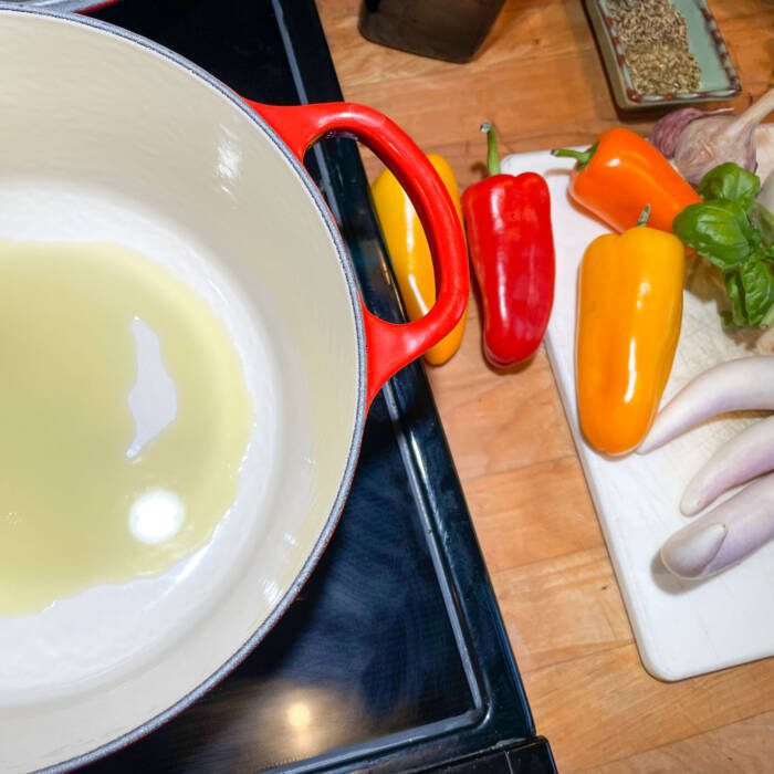 heating oil in a pot with peppers and herbs on a cutting board to the right of the stove