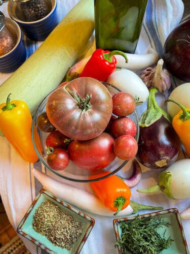 ingredients assembled to make ratatouille including, tomatoes, zucchini, peppers, garlic and herbs