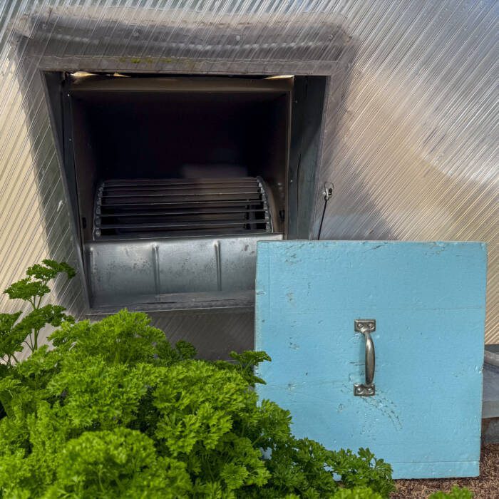 Evaporative cooler on the interior of a Growing Dome greenhouse with a blue board cover propped up next to it that is used in the winter.