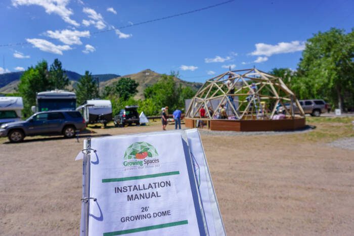printed installation manual being held up in front of an active growing dome greenhouse construction project